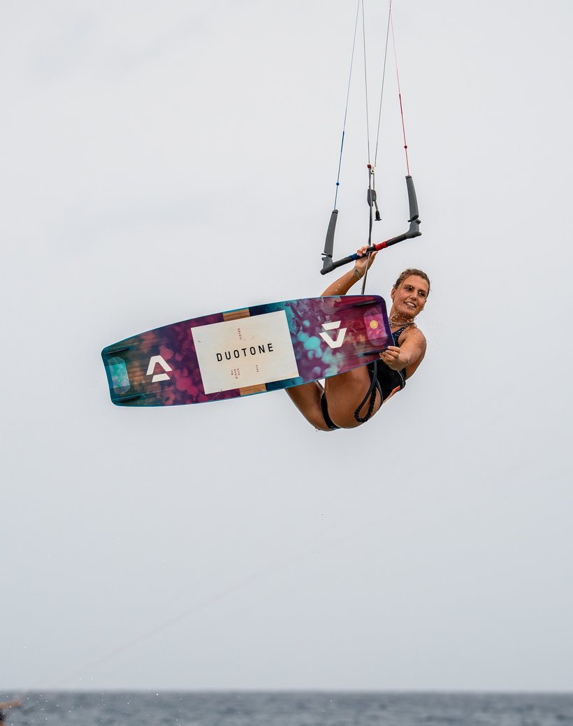Kitesurfer flying through the air with a board grab over turquoise water